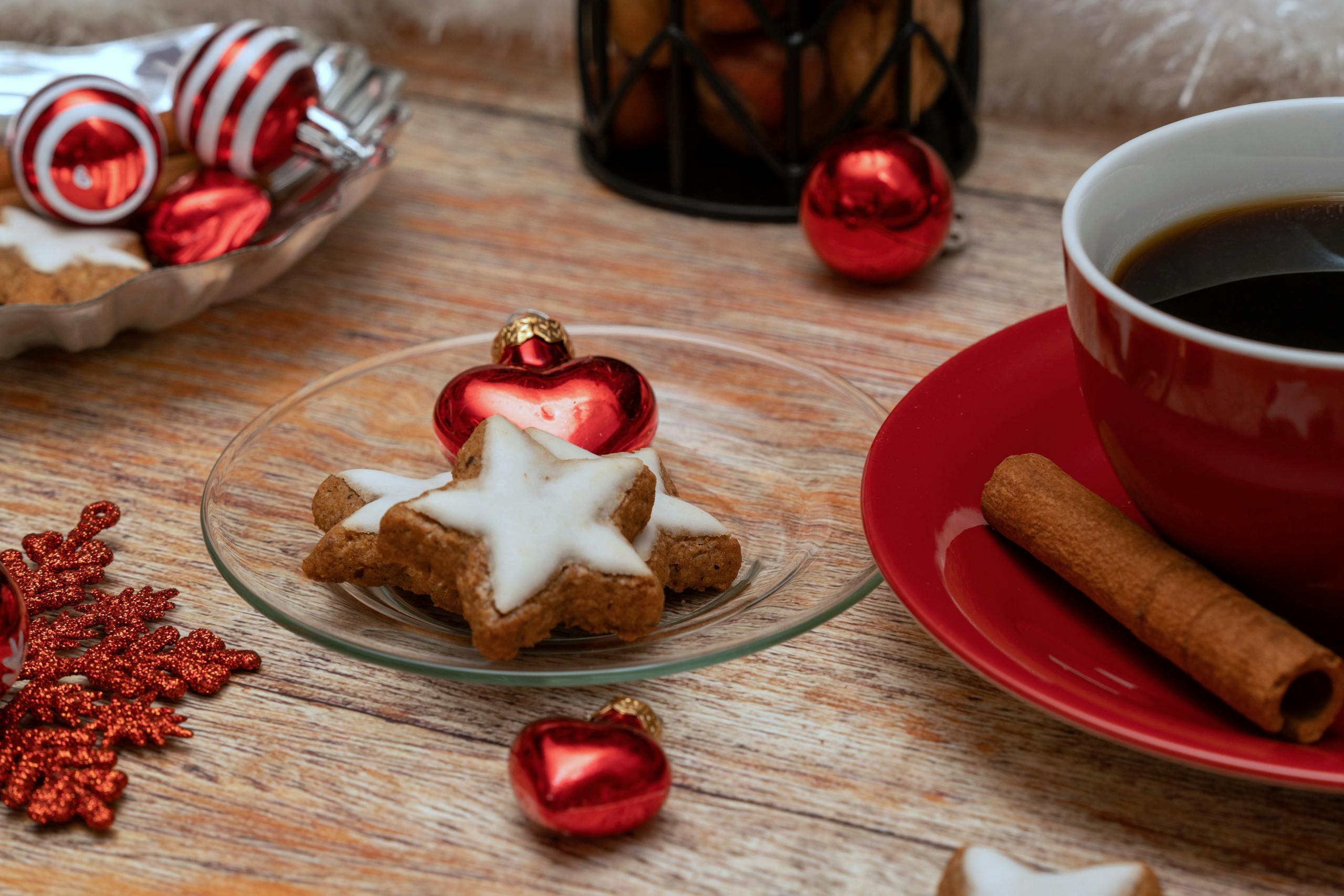 Scène de vacances festive avec des biscuits en forme d'étoile, de la cannelle, du café et des décorations pour une ambiance hivernale chaleureuse.