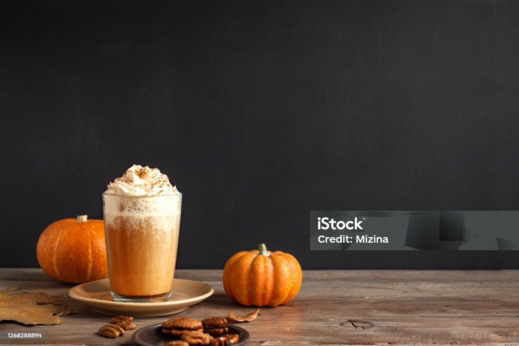 Latte à la citrouille épicée. Boisson caféinée saisonnière et citrouilles biologiques près d'un mur noir, espace pour texte.
