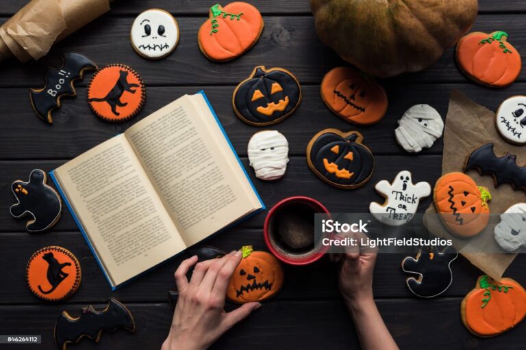 vue de dessus d'une femme lisant un livre et buvant du café entourée de différents biscuits d'Halloween